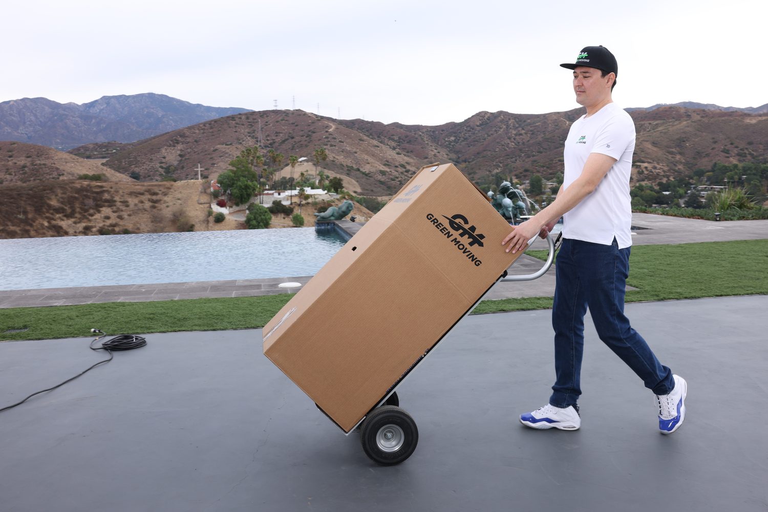 A GreenMoving mover wheeling a box on a hand truck