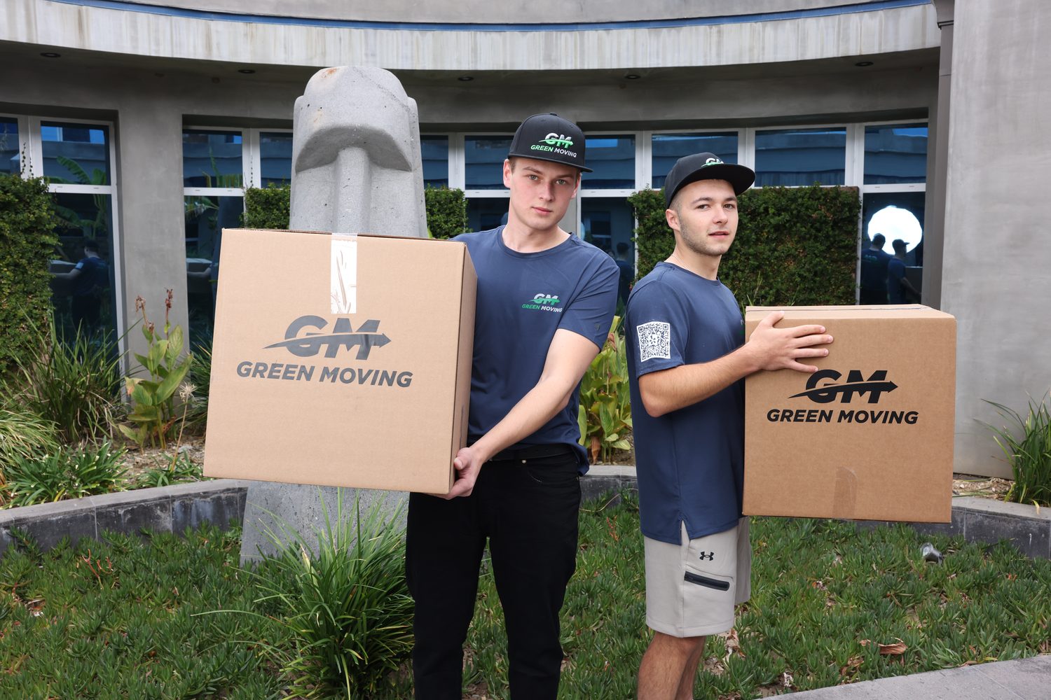 Two GreenMoving movers in uniform carrying a box